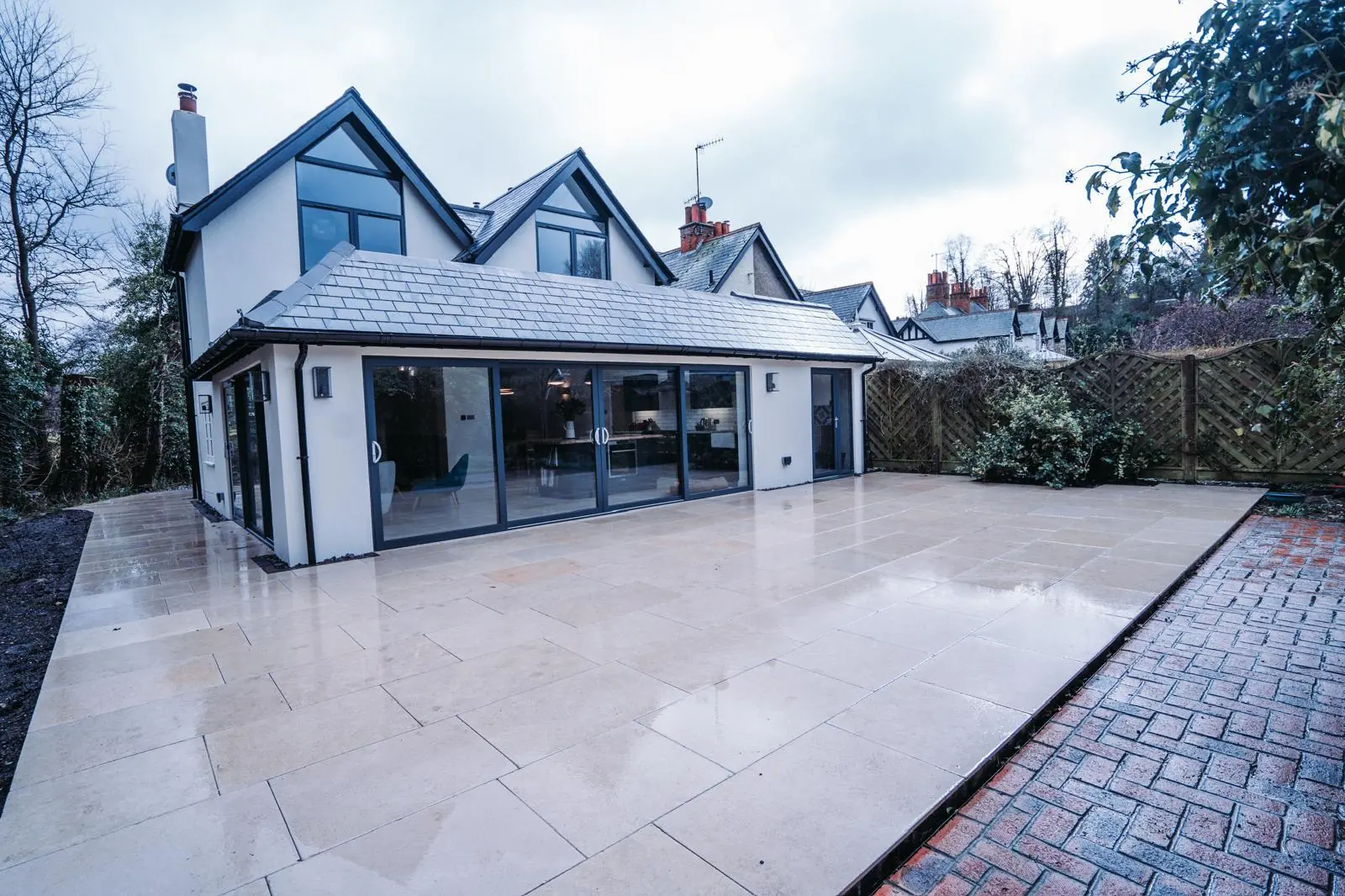 White-rendered home with a glazed rear extension, slate roof and pale paved terrace