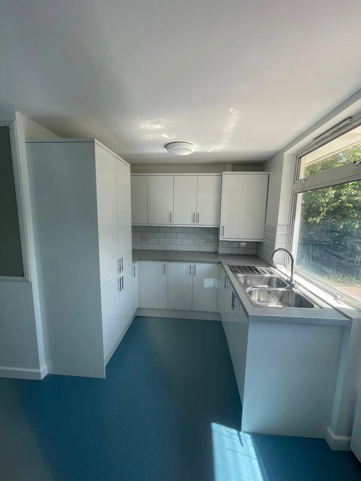 White kitchenette with tiled splashback, double sink and blue flooring