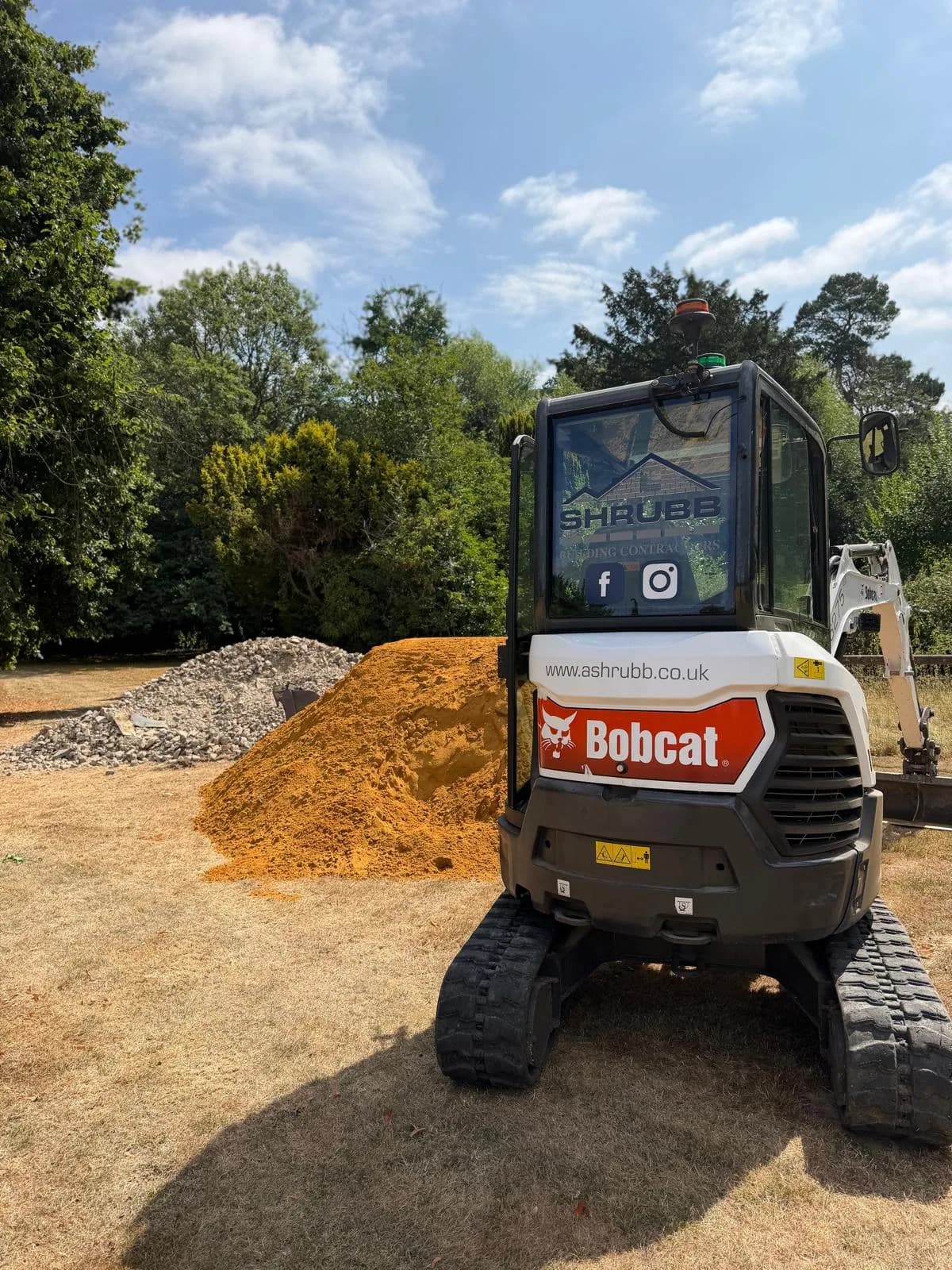 SHRUBB-branded Bobcat digger beside piles of sand and aggregate
